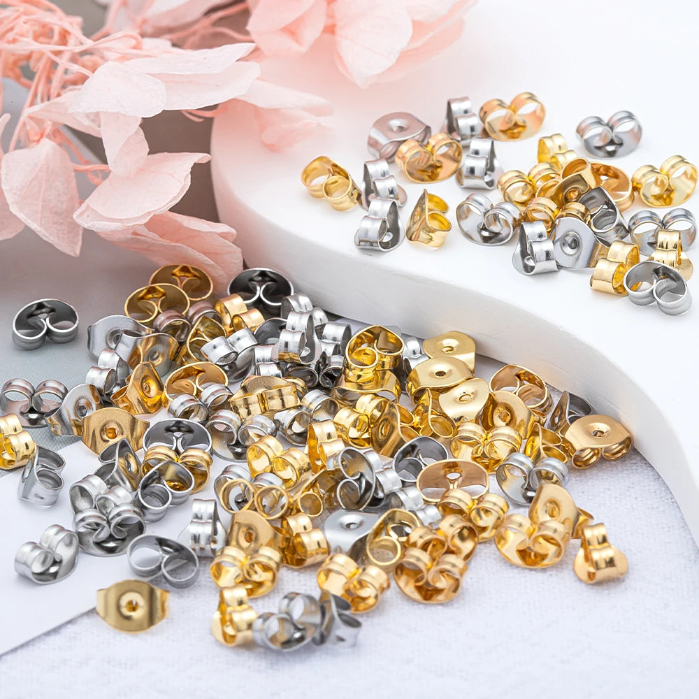 A collection of gold and silver earring stud bases with backs scattered on a white surface.