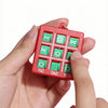 A hand holds a red mini Tic Tac Toe puzzle game with green and white pieces.