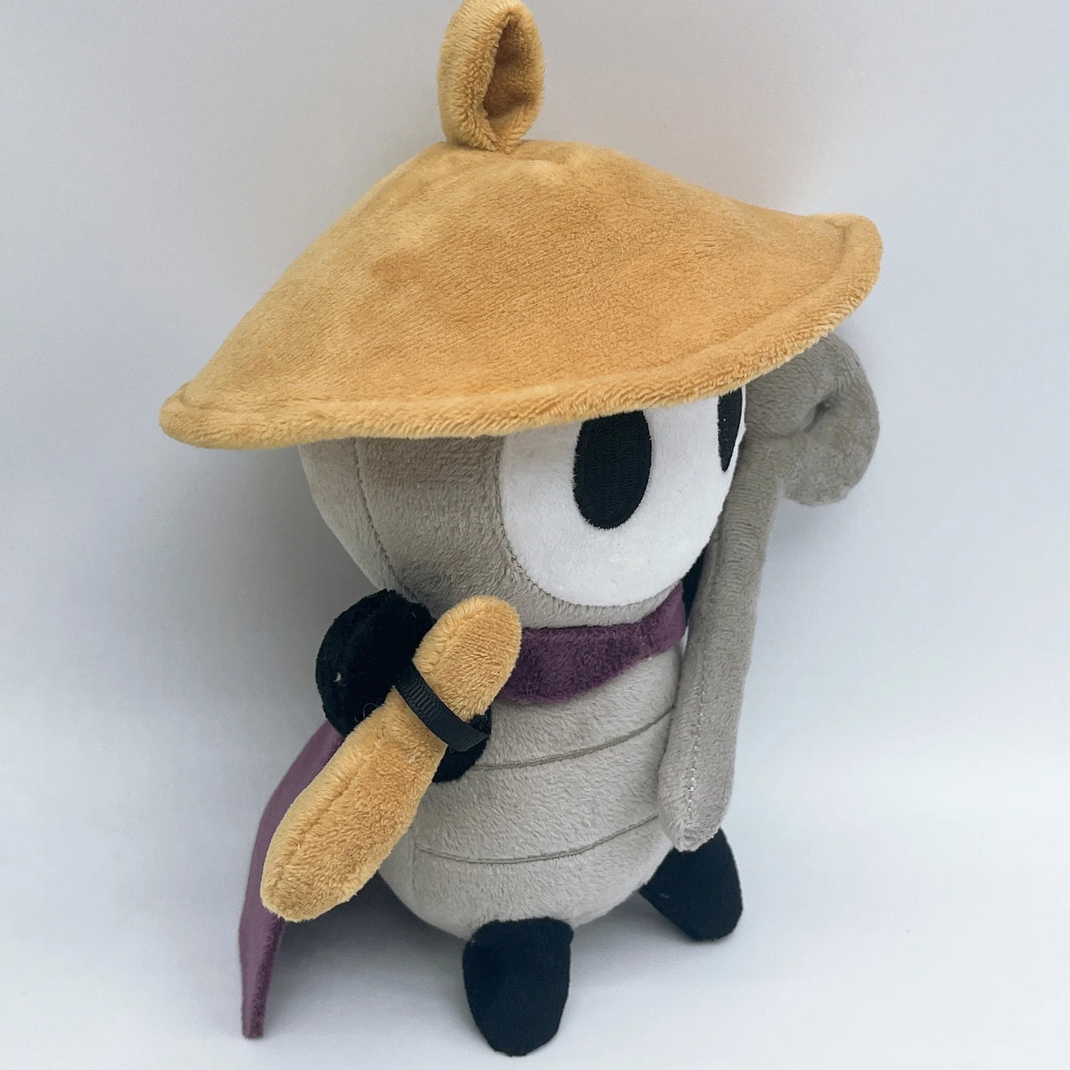 A plush doll resembling Sherma from Hollow Knight Silksong with a tan hat and purple accents.
