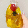 A clear glass bottle filled with yellow liquid and a red object, used as a squishy milk bottle stress ball.