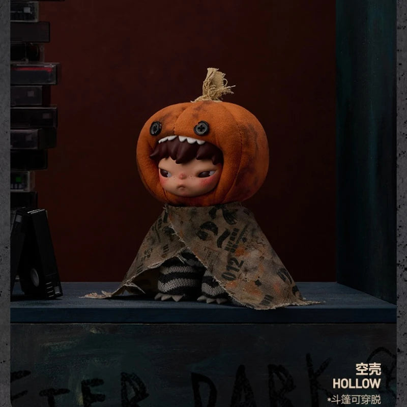 A small, round orange plush doll with a stitched mouth and hair, wearing a patterned fabric, displayed on a dark blue surface