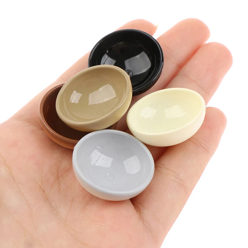 A hand holds a set of ten miniature dollhouse rice bowls in various earthy and light tones.