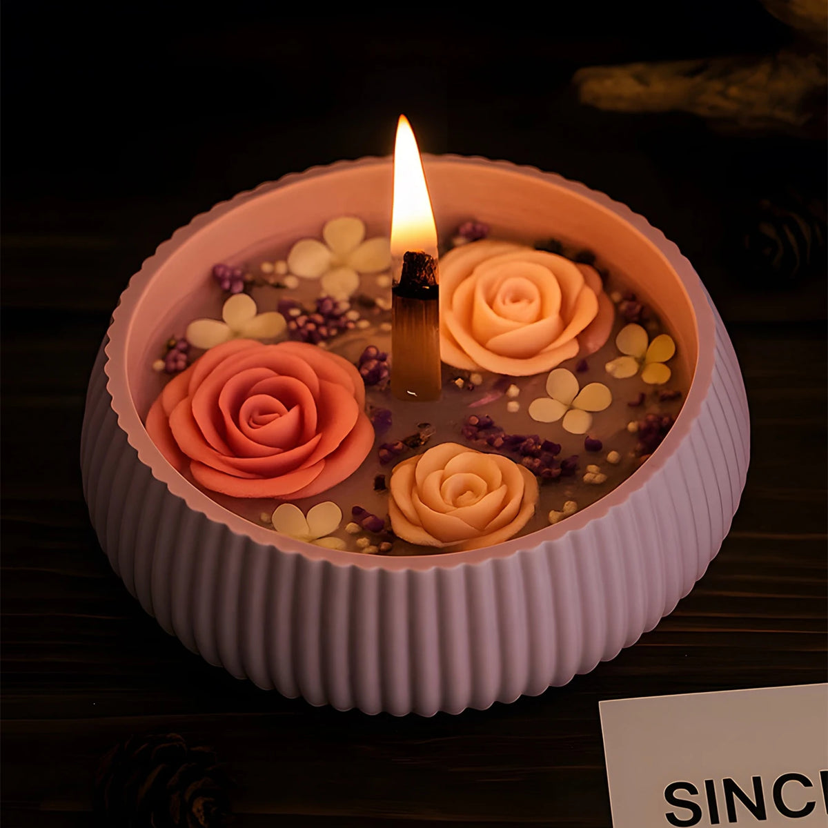 A pink striped silicone mold containing dried flowers and a lit candle for DIY planters and decor.