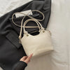 A cream canvas tote bag with light brown leather straps is shown resting on a dark gray blazer.
