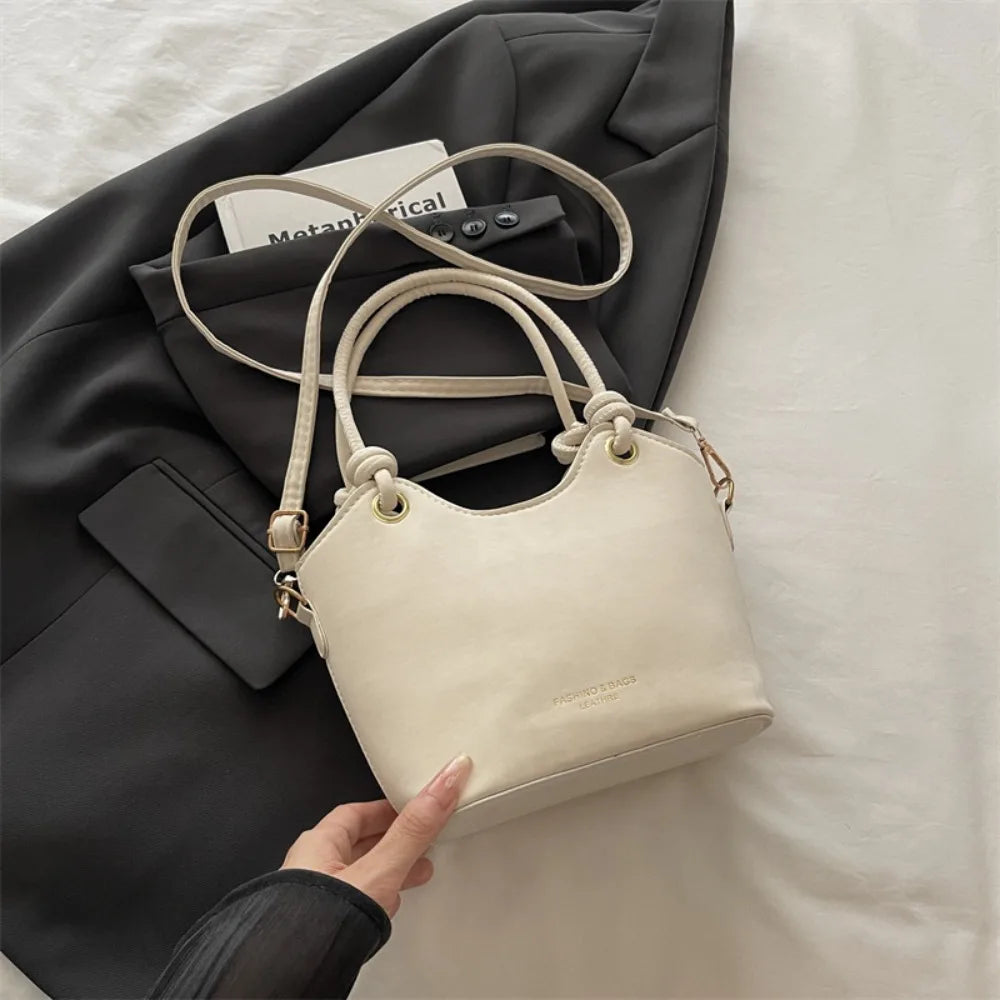 A cream canvas tote bag with light brown leather straps is shown resting on a dark gray blazer.