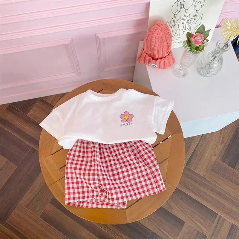 A white t-shirt and red and white checkered shorts set displayed on a wooden tray.