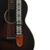 Close-up of an embroidered guitar strap featuring a geometric pattern and leather ends against a dark acoustic guitar body.