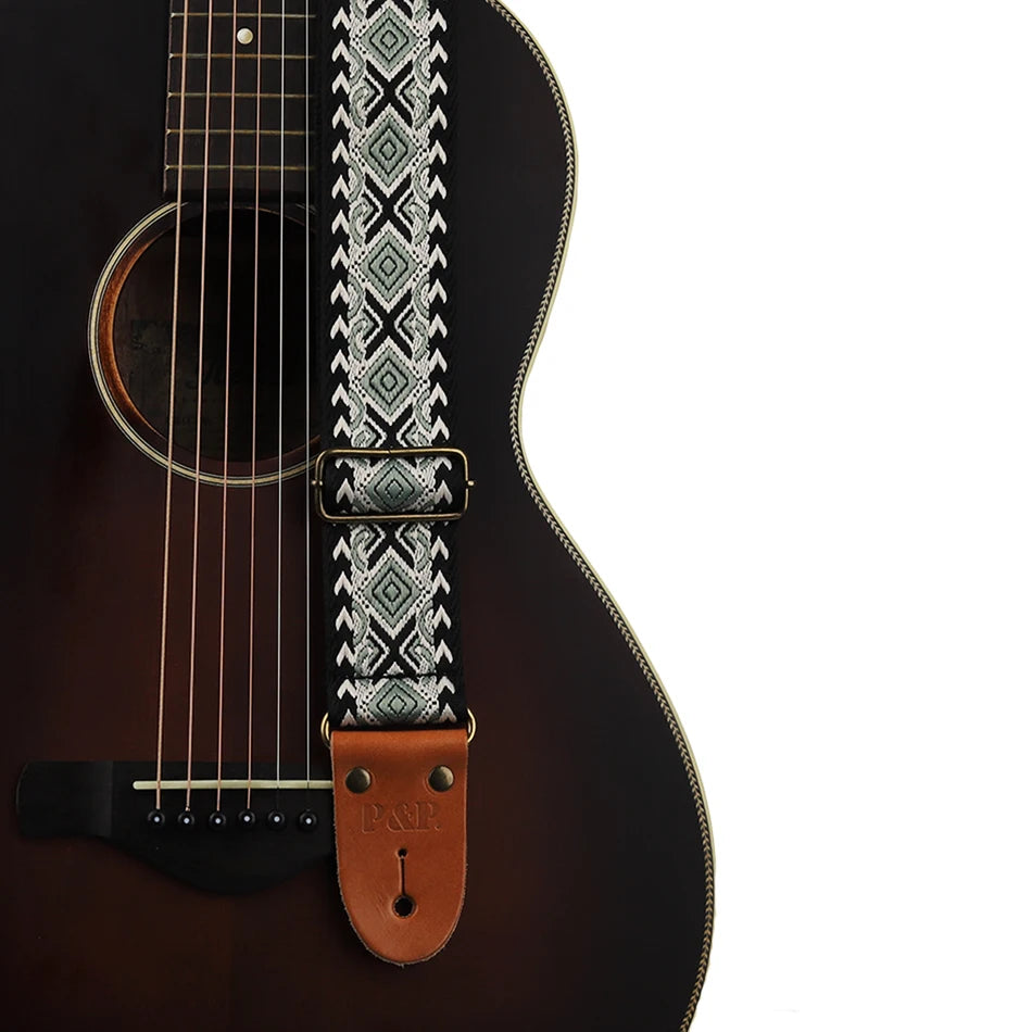 Close-up of an embroidered guitar strap featuring a geometric pattern and leather ends against a dark acoustic guitar body.