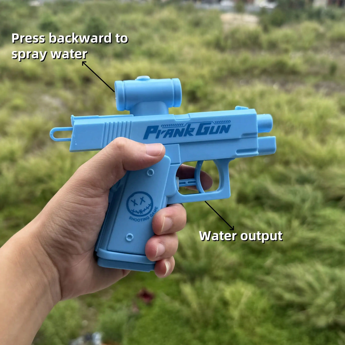A hand holds a blue Plank Gun water gun, demonstrating how to press backward to spray water.