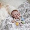 A baby's hand is resting on silicone baby teether with various colored chew beads on a patterned fabric.