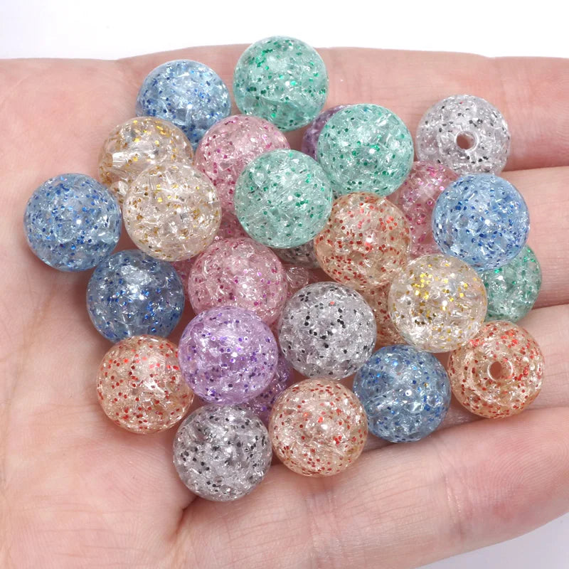 A hand holds a pile of colorful glitter cracked acrylic round beads for jewelry making