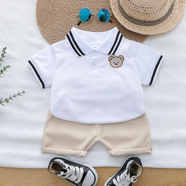 A white polo shirt and beige shorts set for toddlers with a bear embroidery, displayed on a light background.