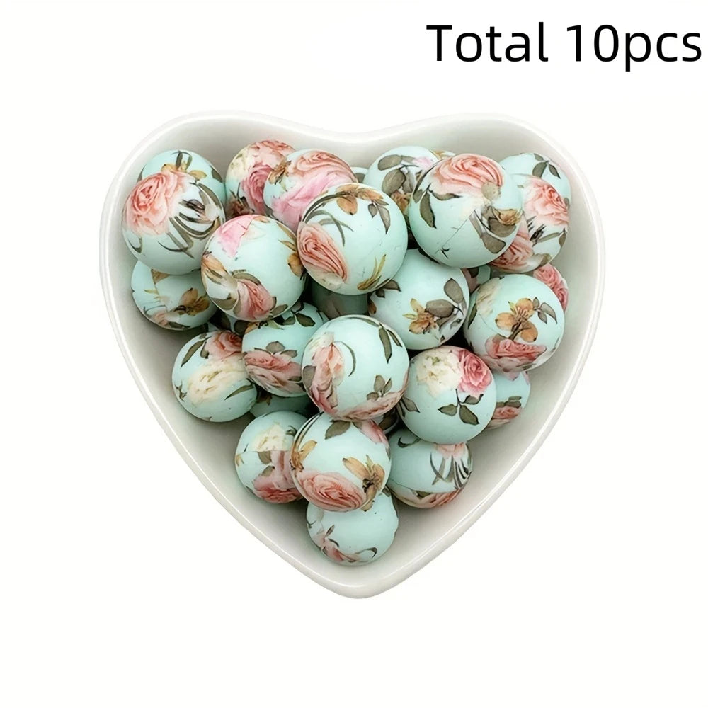 A heart-shaped dish filled with ten pink and green floral printed silicone beads for DIY jewelry making