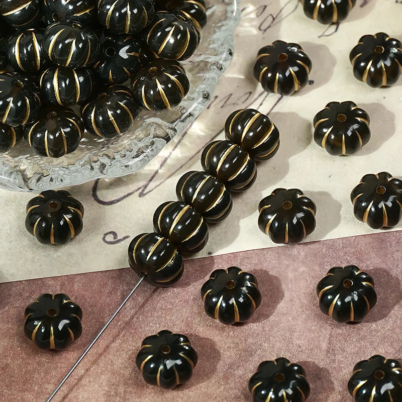 A collection of small, dark resin pumpkin beads with gold tracing marks arranged on a light surface.