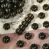 A collection of small, dark resin pumpkin beads with gold tracing marks arranged on a clear glass dish.