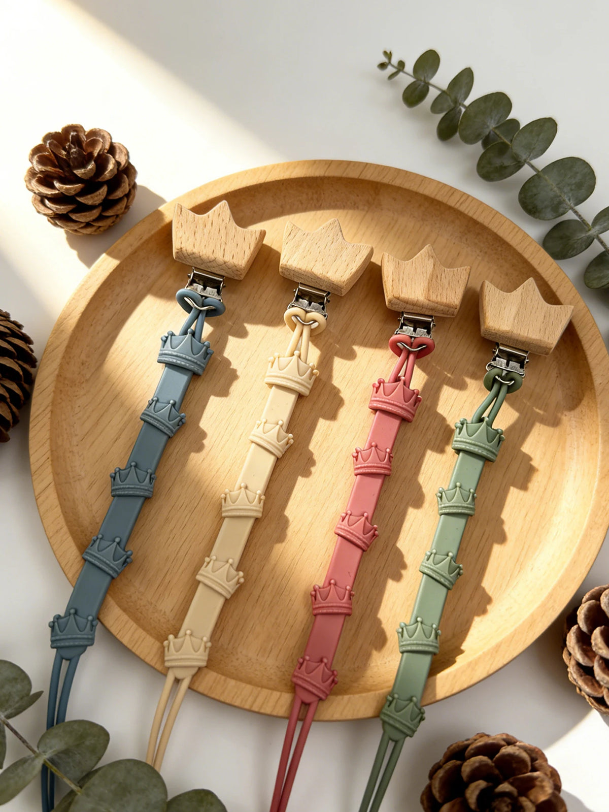 A set of baby pacifier clips in various pastel colors, including blue, beige, pink, and green, displayed on a wooden plate.