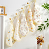 A set of five white and yellow patterned soft cotton muslin baby washcloths hanging on a light wooden rack.