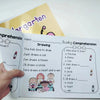 A hand holds an interactive English reading comprehension book showing drawings and questions for children.