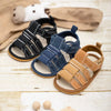 A set of soft non-slip baby sandals for first walkers in various earthy tones including black, blue, and tan.