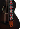 Close-up of an embroidered guitar strap featuring a geometric pattern and leather ends attached to a dark acoustic guitar bod