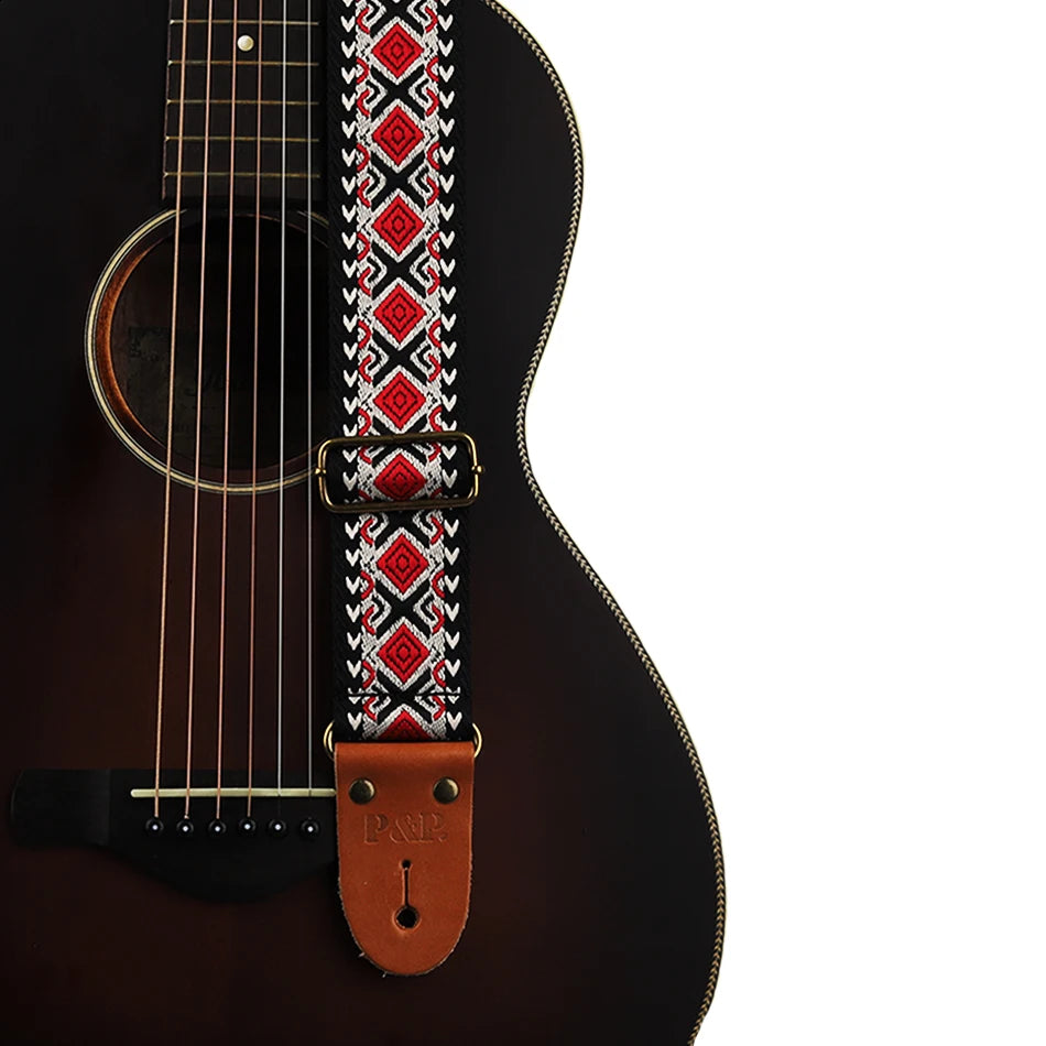Close-up of an embroidered guitar strap featuring a geometric pattern and leather ends attached to a dark acoustic guitar bod