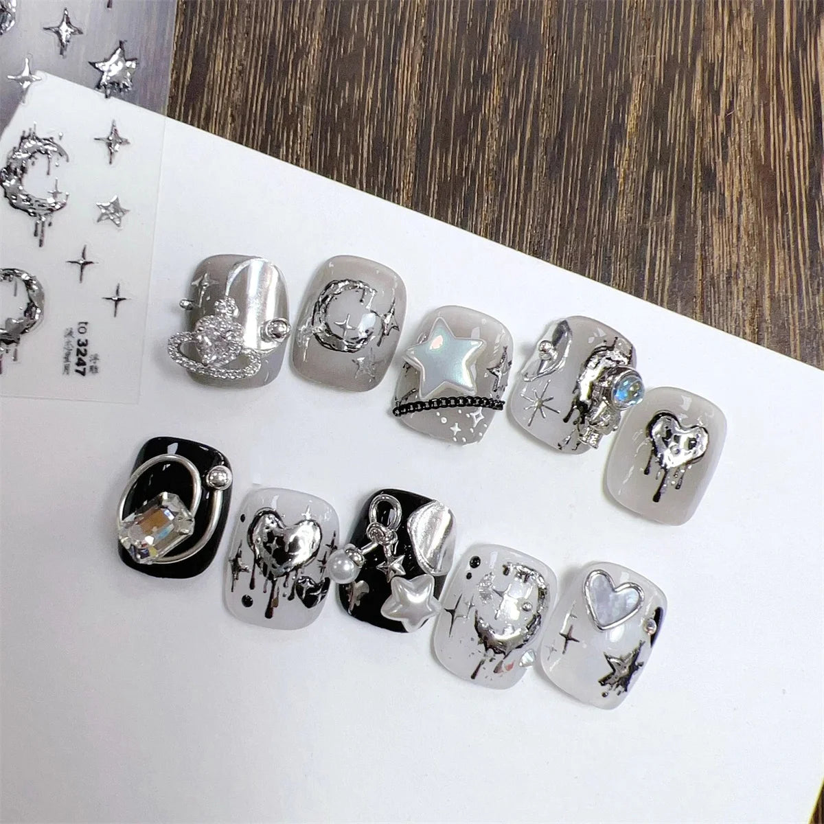 A collection of silver and black gothic nail art stickers featuring stars, skulls, and other dark motifs on a white backgroun