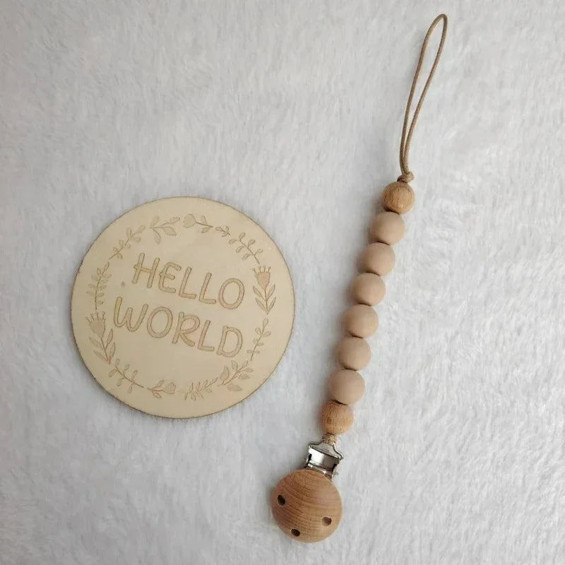 A wooden bead pacifier clip with a silicone teether on a natural fiber string and a circular wooden sign that reads Hello Wor