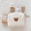 A quilted white baby diaper caddy organizer with a handle and attached stroller straps is shown on a light background.