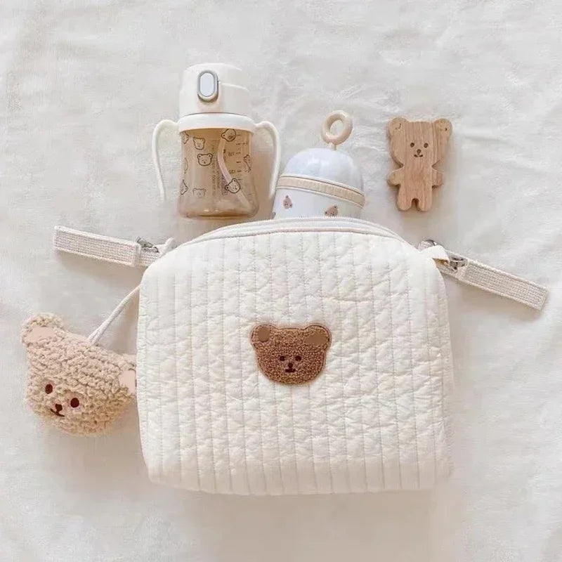 A quilted white baby diaper caddy organizer with a handle and attached stroller straps is shown on a light background.