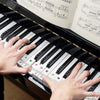A hand plays a piano keyboard with note stickers on white and black keys.