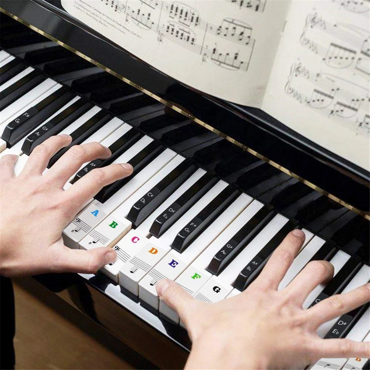 A hand plays a piano keyboard with note stickers on white and black keys.