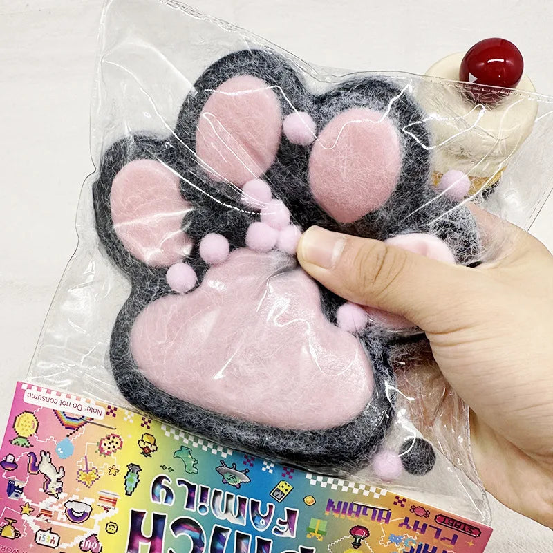 A pink and black giant cat paw squishy stress relief toy is shown being held by a hand.