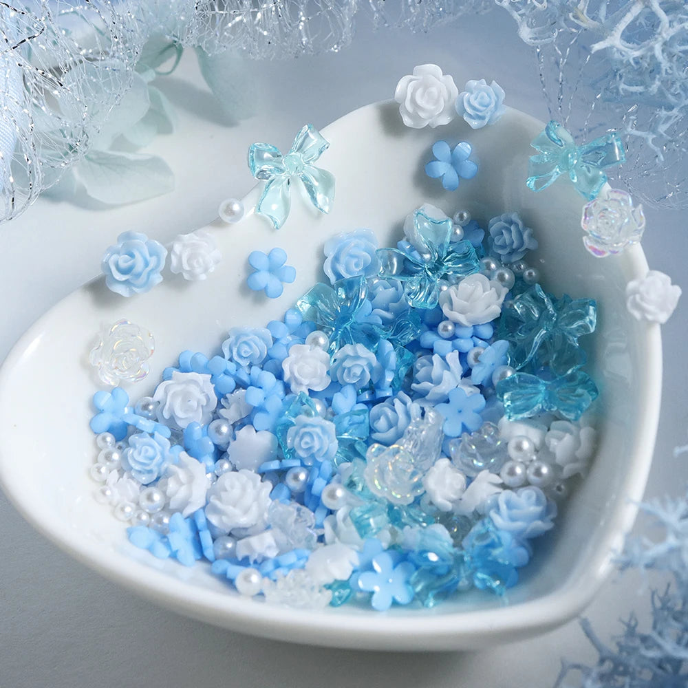 A white dish filled with blue and white camellia bowknot resin shakers and fillers surrounded by silver tinsel.