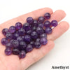 A handful of round purple amethyst beads resting on a person's palm.