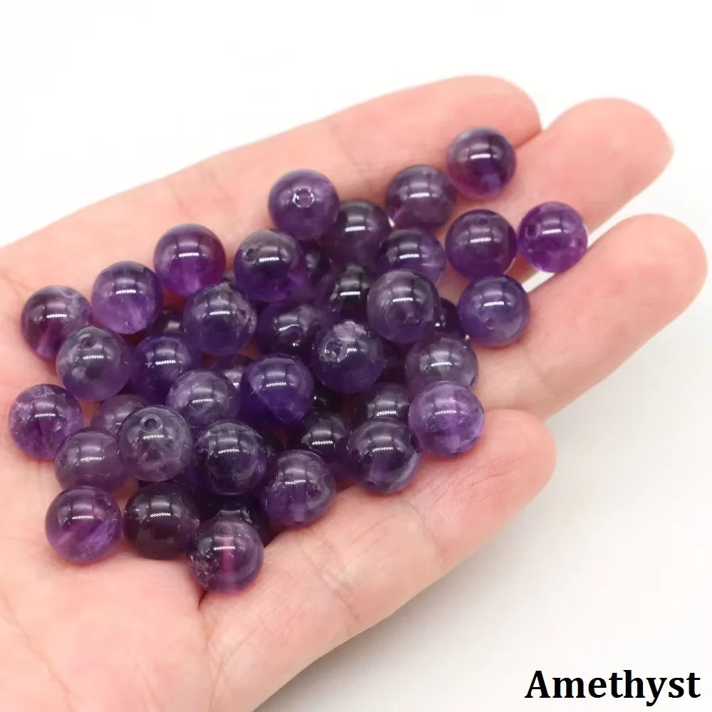 A handful of round purple amethyst beads resting on a person's palm.