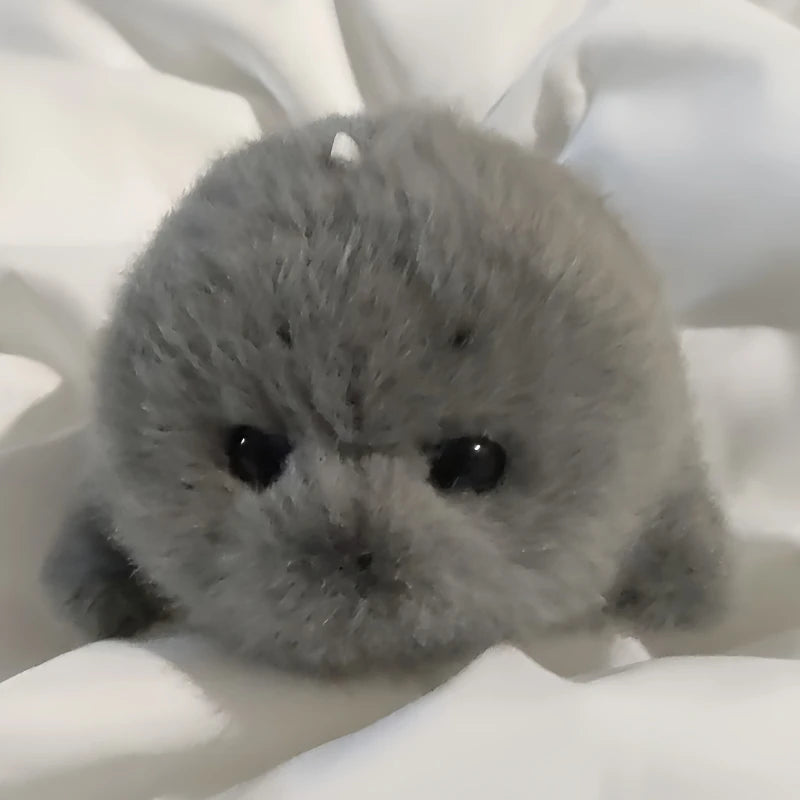 A small, round grey seal plush toy resting on a white surface.