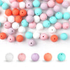 A variety of round silicone beads in pastel and bright colors are scattered across a white surface.