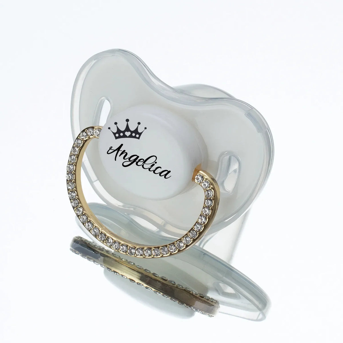 A clear silicone baby pacifier with a crown design and the name Angelica engraved in rhinestone lettering.
