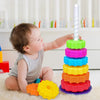 A baby is interacting with a colorful rainbow spin tower stacking toy made of plastic rings.