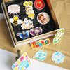 A gold-edged box filled with ten autumn pumpkin flatback resin décor items including bees, flowers, and leaves.