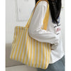 Une femme tient un sac cabas à l'épaule rayé jaune et blanc contre un t-shirt blanc.