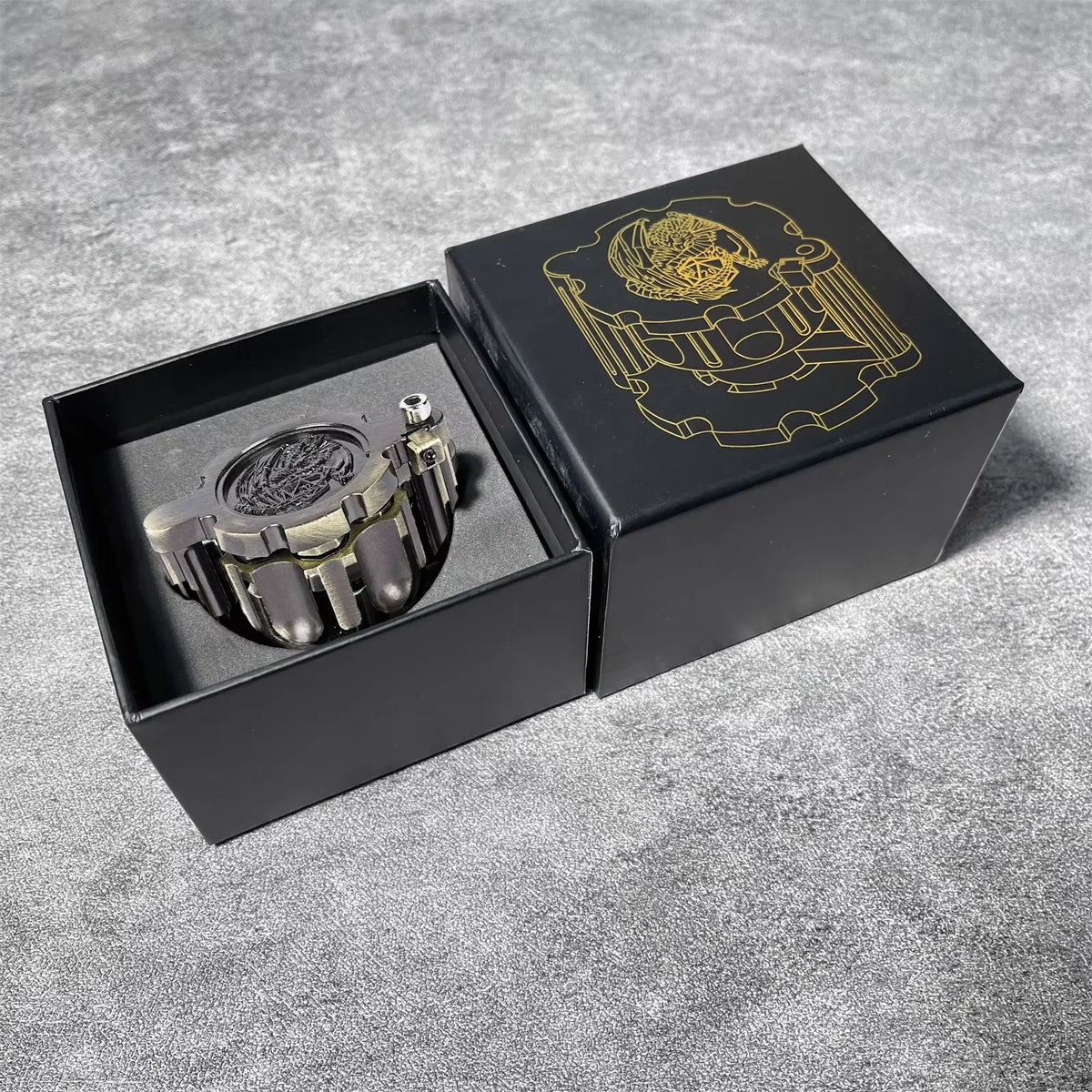 A black box containing a revolver-shaped metal dice set for RPG games with gold accents.