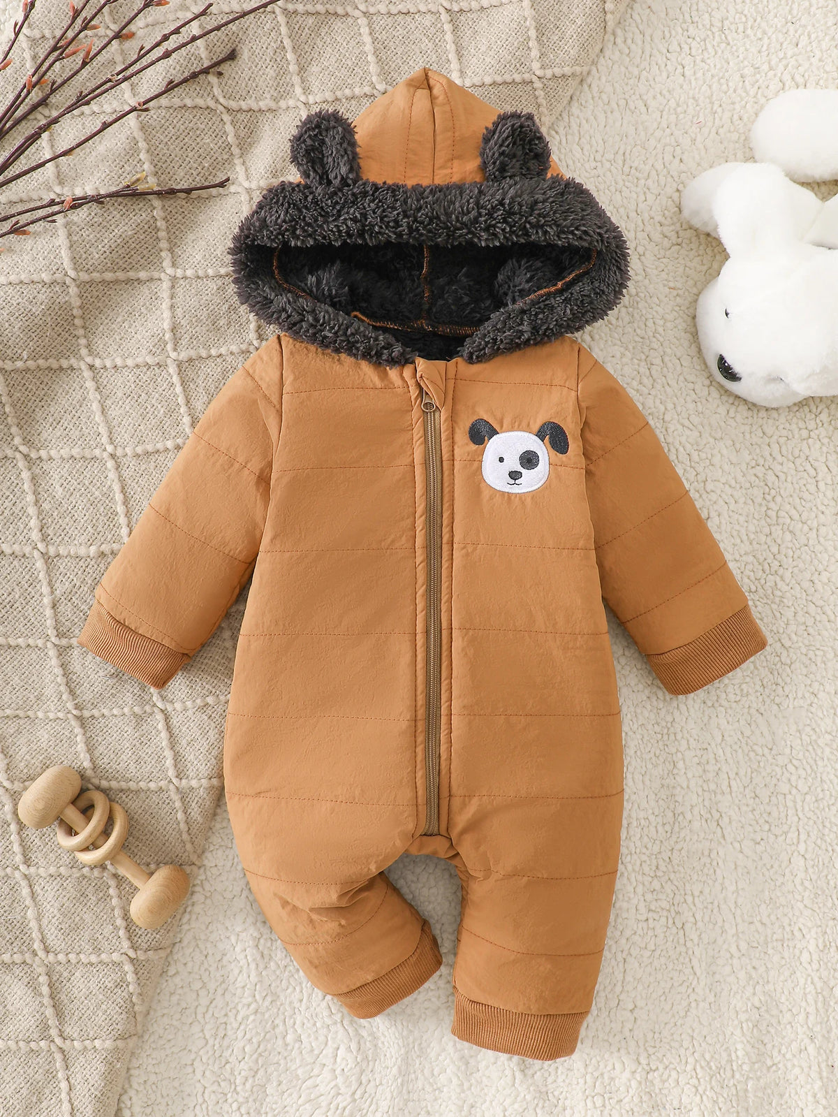 A brown fleece romper for infants with a gray fur hood and a white panda face detail, lying on a cream textured fabric.