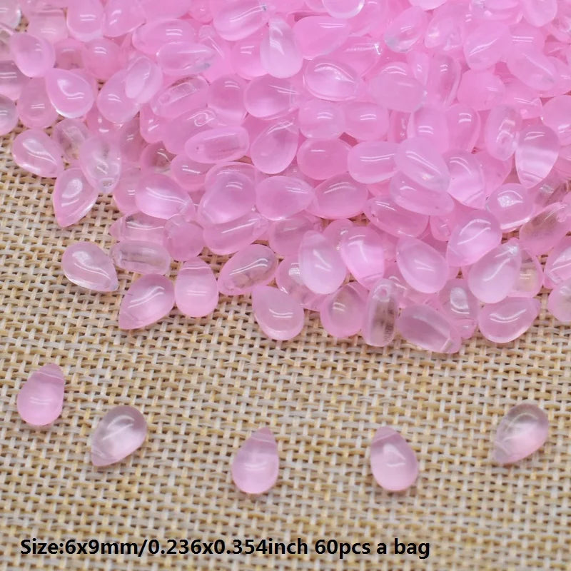 Pink water drop glass beads for jewelry making laid out on a woven fabric