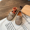 A pair of tan suede girls' moccasins with bow details resting on a white paper with wine tasting notes.