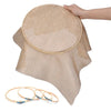 A hand is placing a bamboo embroidery hoop onto a piece of beige fabric, with several hoops lying nearby.