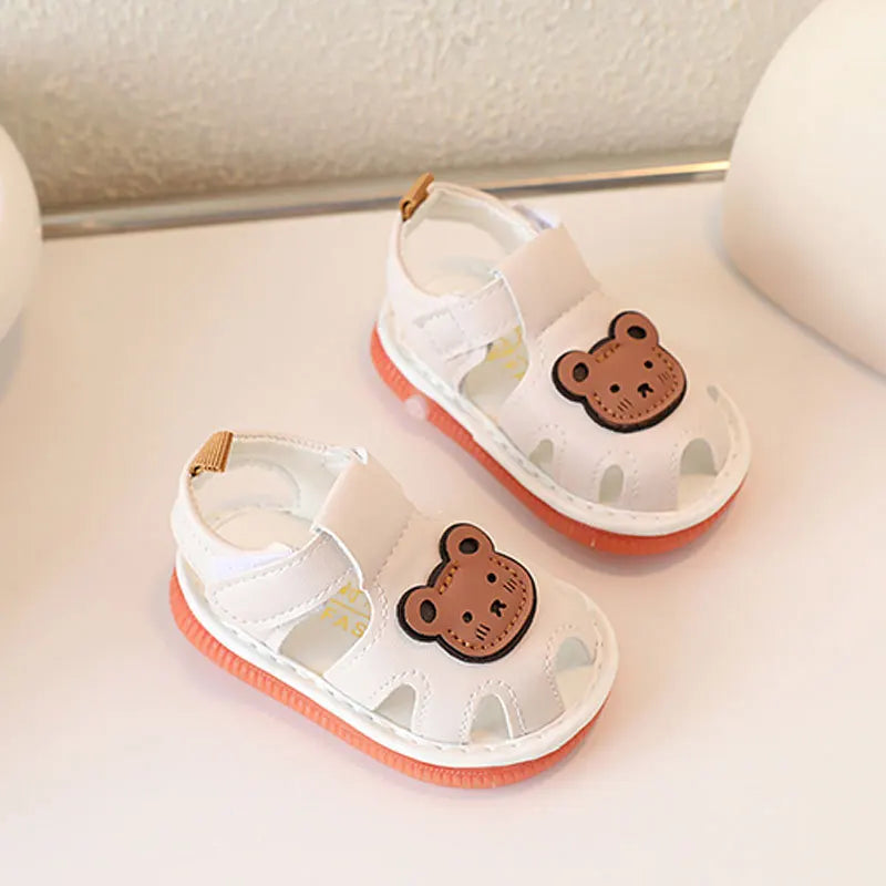 Une paire de sandales d'été blanches antidérapantes pour bébés avec un motif ours brun sur l'avant-pied.