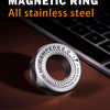 A silver magnetic ring with etched text rests on a dark surface next to a laptop keyboard.