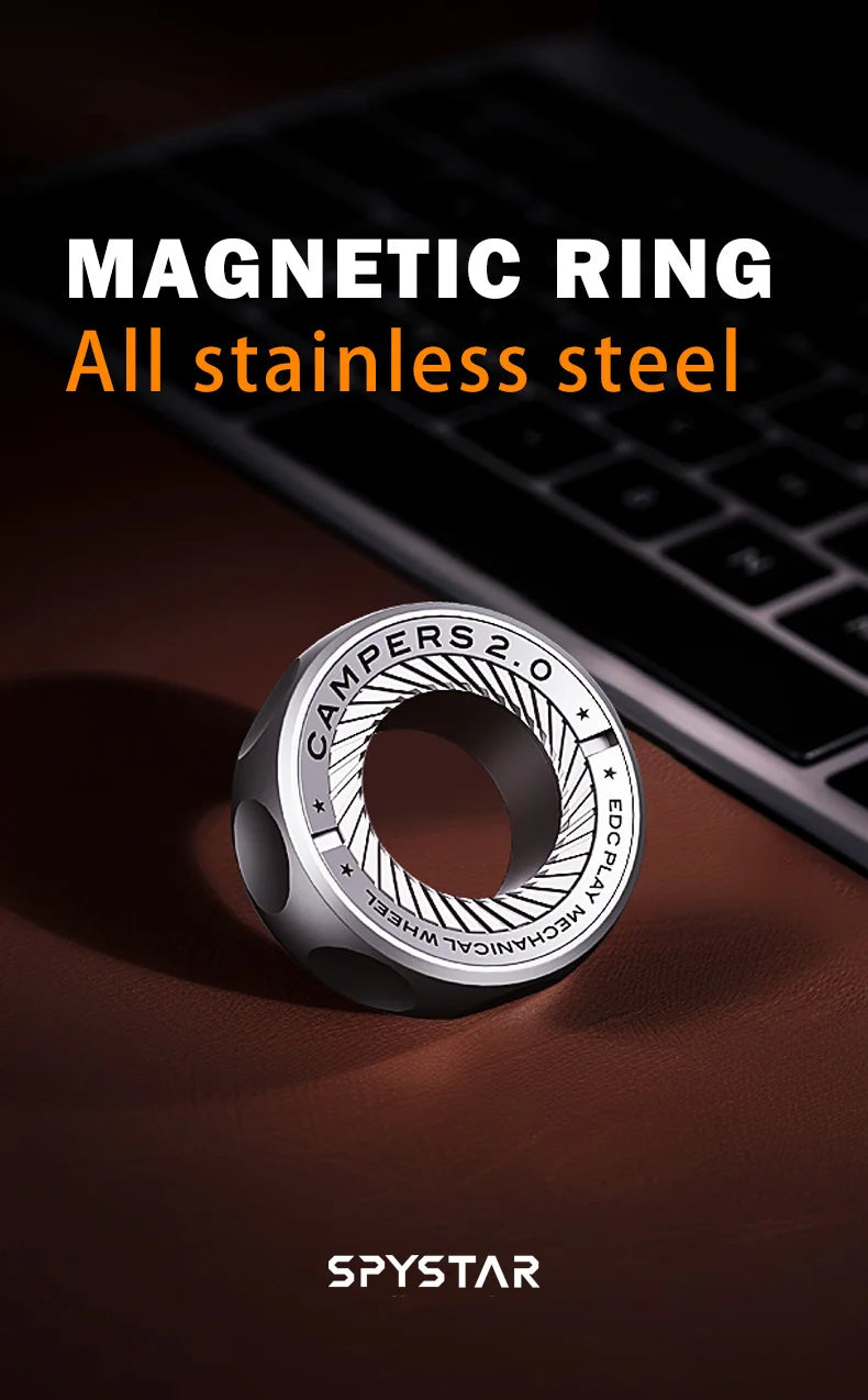 A silver magnetic ring with etched text rests on a dark surface next to a laptop keyboard.