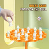 A board game setup featuring small white frog figures on an orange tree, with a hand reaching toward the game.